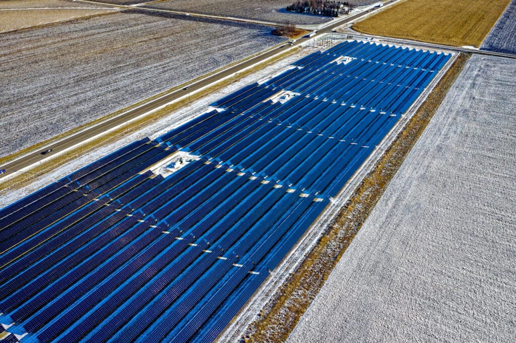 Aerial shot of expansive solar panel installation in snowy fields during daylight in Claremont, MN.