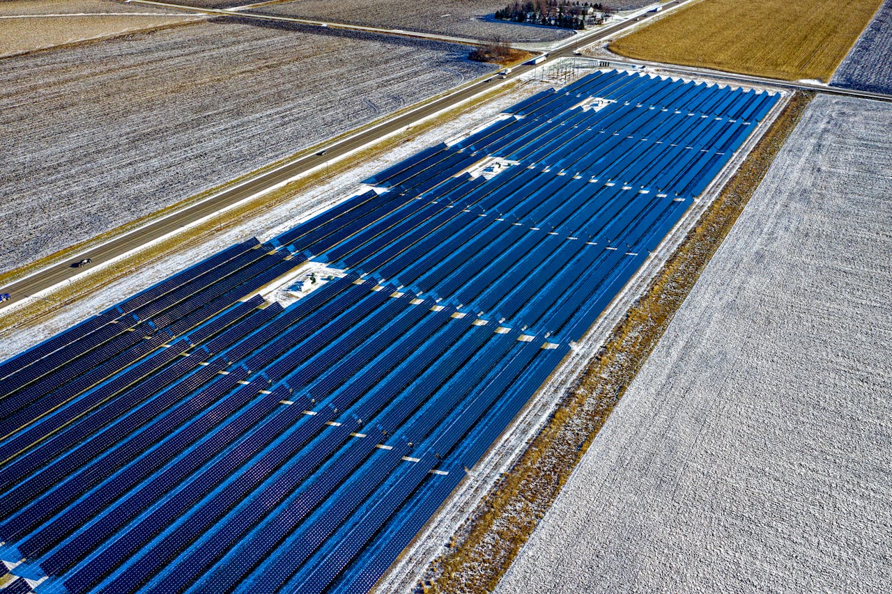 Aerial shot of expansive solar panel installation in snowy fields during daylight in Claremont, MN.
